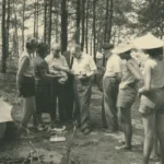Gruppe von Personen betrachtet archäologische Funde im Freien, umgeben von Bäumen, vermutlich im Emsland der 1950er Jahre.