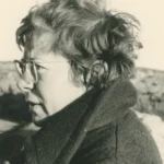 Schwarzweißfoto von Dr. Elisabeth Schlicht im Profil, mit Brille und kurzem lockigem Haar, in einem Wollmantel im Freien.