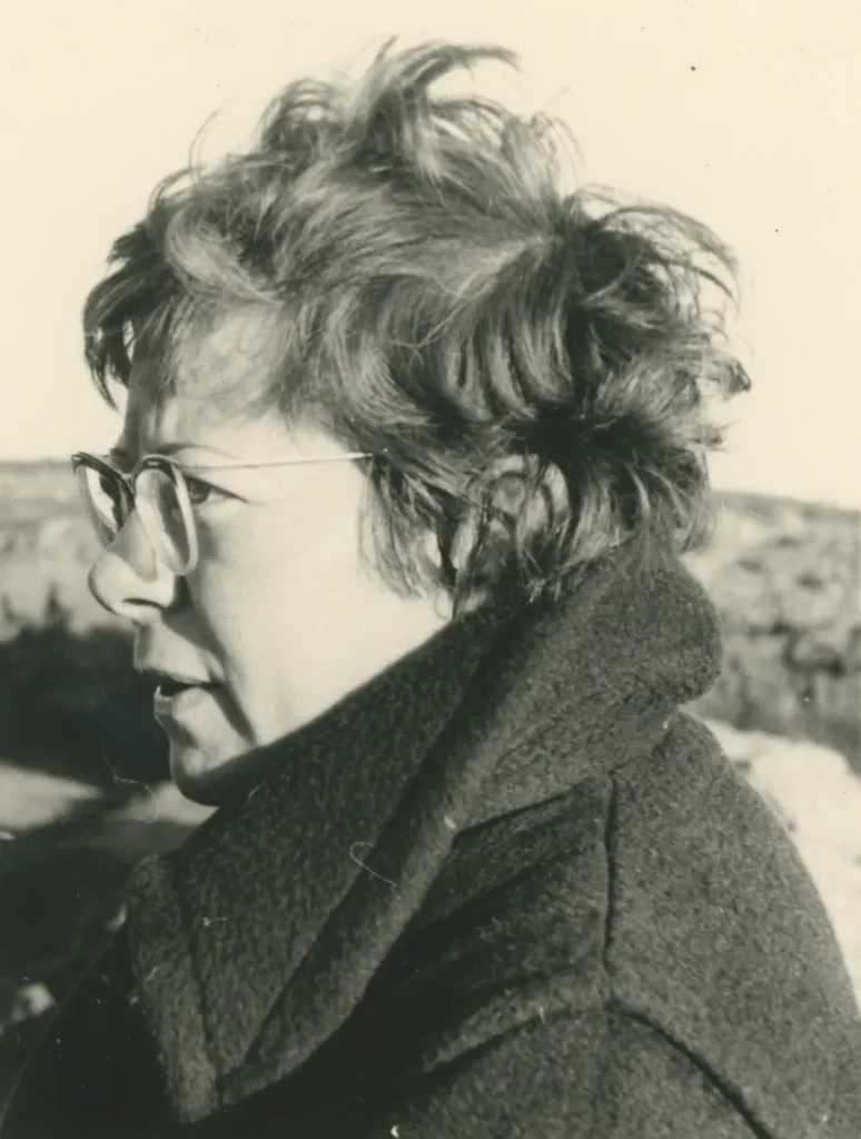Schwarzweißfoto von Dr. Elisabeth Schlicht im Profil, mit Brille und kurzem lockigem Haar, in einem Wollmantel im Freien.