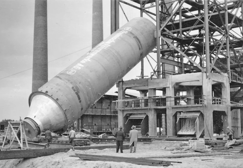 Arbeiter beobachten das Einsetzen eines riesigen zylindrischen Industriebauteils auf der Baustelle der Raffinerie Lingen.