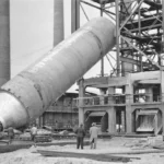 Arbeiter beobachten das Einsetzen eines riesigen zylindrischen Industriebauteils auf der Baustelle der Raffinerie Lingen.