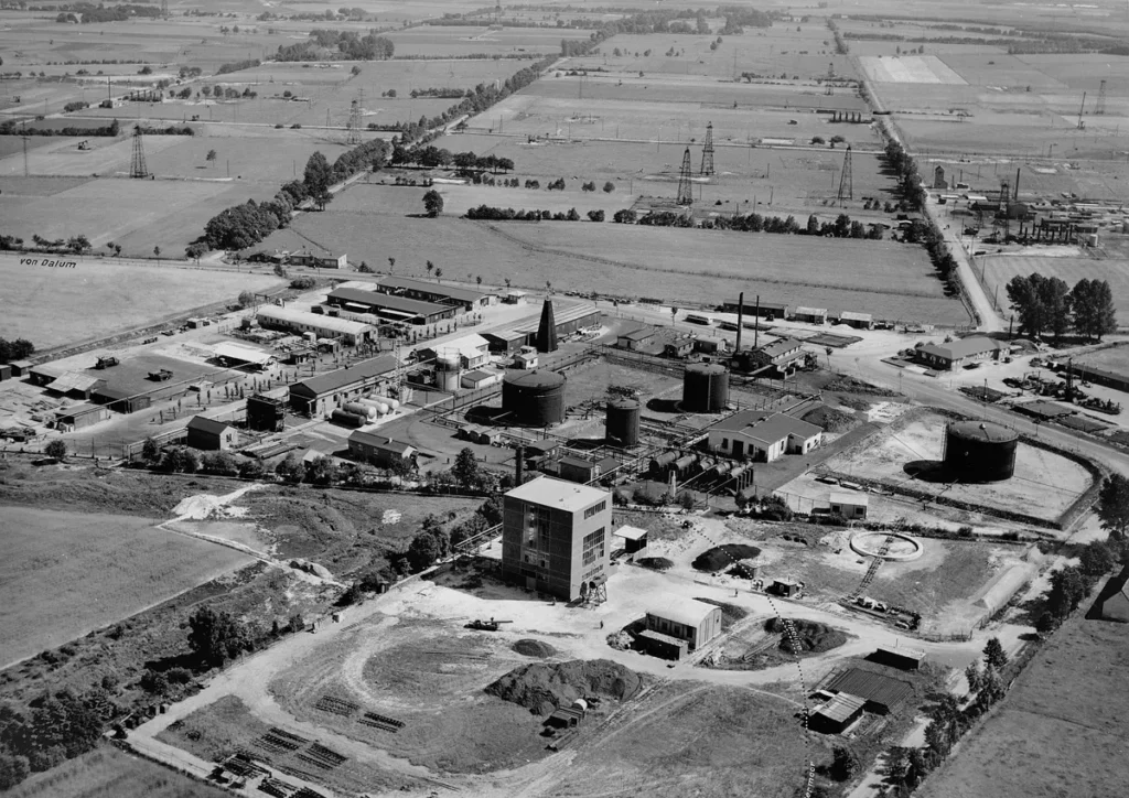 Luftaufnahme einer Erdölförderanlage mit Tanks, Bohrtürmen und Industriegebäuden in flacher Moorlandschaft.