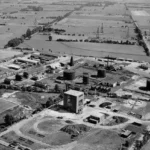 Luftaufnahme einer Erdölförderanlage mit Tanks, Bohrtürmen und Industriegebäuden in flacher Moorlandschaft.