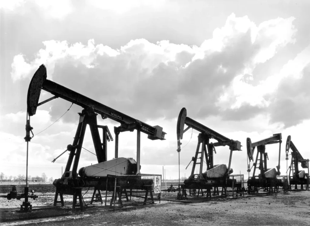 Fünf Pumpjacks einer Erdölförderanlage im Emsland stehen in einer Reihe unter bewölktem Himmel, 1950er Jahre.