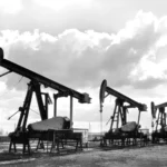 Fünf Pumpjacks einer Erdölförderanlage im Emsland stehen in einer Reihe unter bewölktem Himmel, 1950er Jahre.