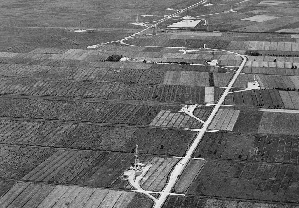 Luftaufnahme einer flachen Moorlandschaft mit Erdölbohrturm, Versorgungsstraßen und landwirtschaftlichen Feldern im Emsland.