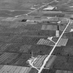 Luftaufnahme einer flachen Moorlandschaft mit Erdölbohrturm, Versorgungsstraßen und landwirtschaftlichen Feldern im Emsland.