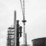 Schwarzweißfoto des Baus der Raffinerie Lingen mit Kran, Destillationsturm und Stahlgerüst, ca. 1950er Jahre.