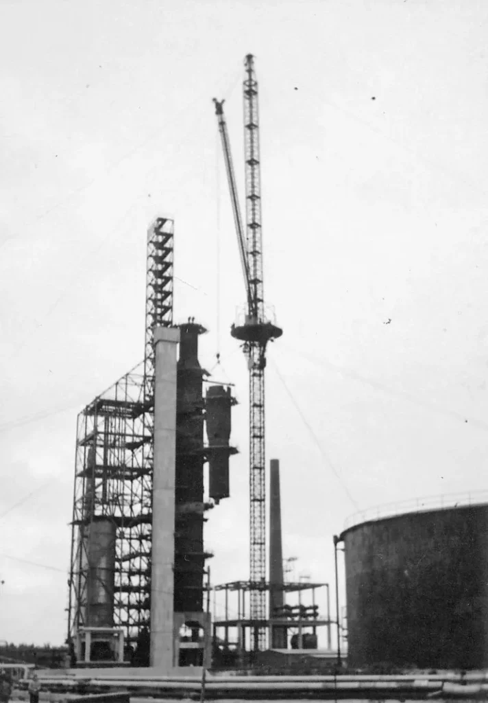 Schwarzweißfoto des Baus der Raffinerie Lingen mit Kran, Destillationsturm und Stahlgerüst, ca. 1950er Jahre.