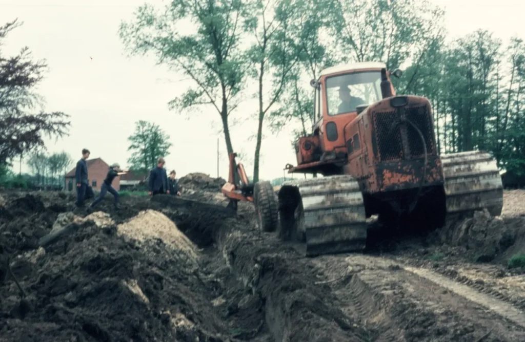 Ein orangefarbener Bulldozer planiert schlammiges Gelände, begleitet von mehreren Arbeitern bei Flurbereinigungsarbeiten im Emsland.