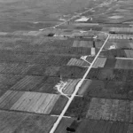 Historische Schwarzweiß-Luftaufnahme von Erdölförderanlagen mit Bohrtürmen inmitten landwirtschaftlicher Felder im Emsland.
