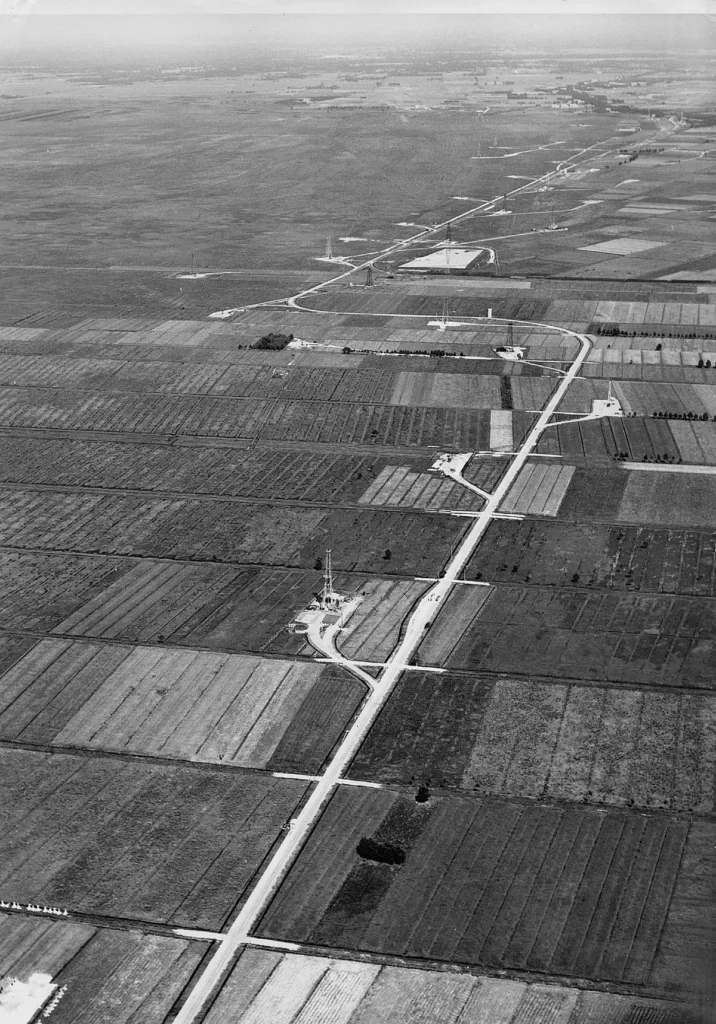 Historische Schwarzweiß-Luftaufnahme von Erdölförderanlagen mit Bohrtürmen inmitten landwirtschaftlicher Felder im Emsland.