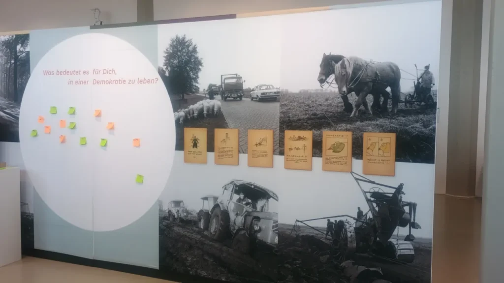 Museumsausstellung mit historischen Schwarzweißfotos landwirtschaftlicher Szenen und Infokarten zu niederländischen Annexionsplänen nach 1945.