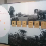 Museumsausstellung mit historischen Schwarzweißfotos landwirtschaftlicher Szenen und Infokarten zu niederländischen Annexionsplänen nach 1945.