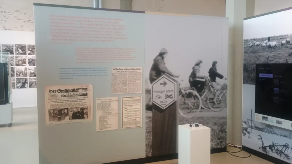 Museumsausstellung mit historischen Zeitungsartikeln, einem Wegweiser der Hesinger Grenzroute und einem Schwarzweißfoto von Radfahrern.