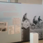 Museumsausstellung mit historischen Zeitungsartikeln, einem Wegweiser der Hesinger Grenzroute und einem Schwarzweißfoto von Radfahrern.