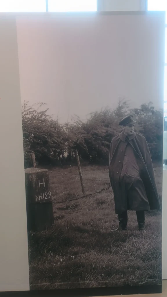 Ein uniformierter Mann steht neben einem Grenzstein mit der Aufschrift H Nr. 129 an der deutsch-niederländischen Grenze.