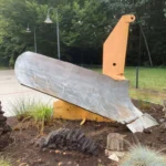 Gelber Baggerarm mit Schaufel als Freilicht-Denkmal in einem gepflegten Garten, Symbol der Moorerschließung.
