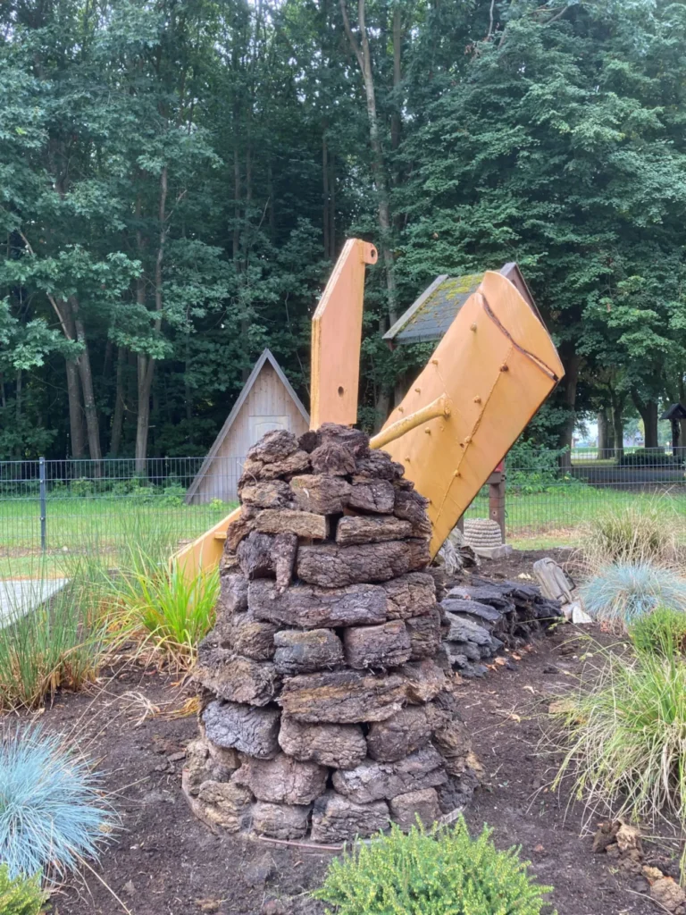 Ein Kunstwerk aus gestapelten Torfblöcken mit einem gelben Pflugschild symbolisiert die Moorkolonisierung im Emsland.