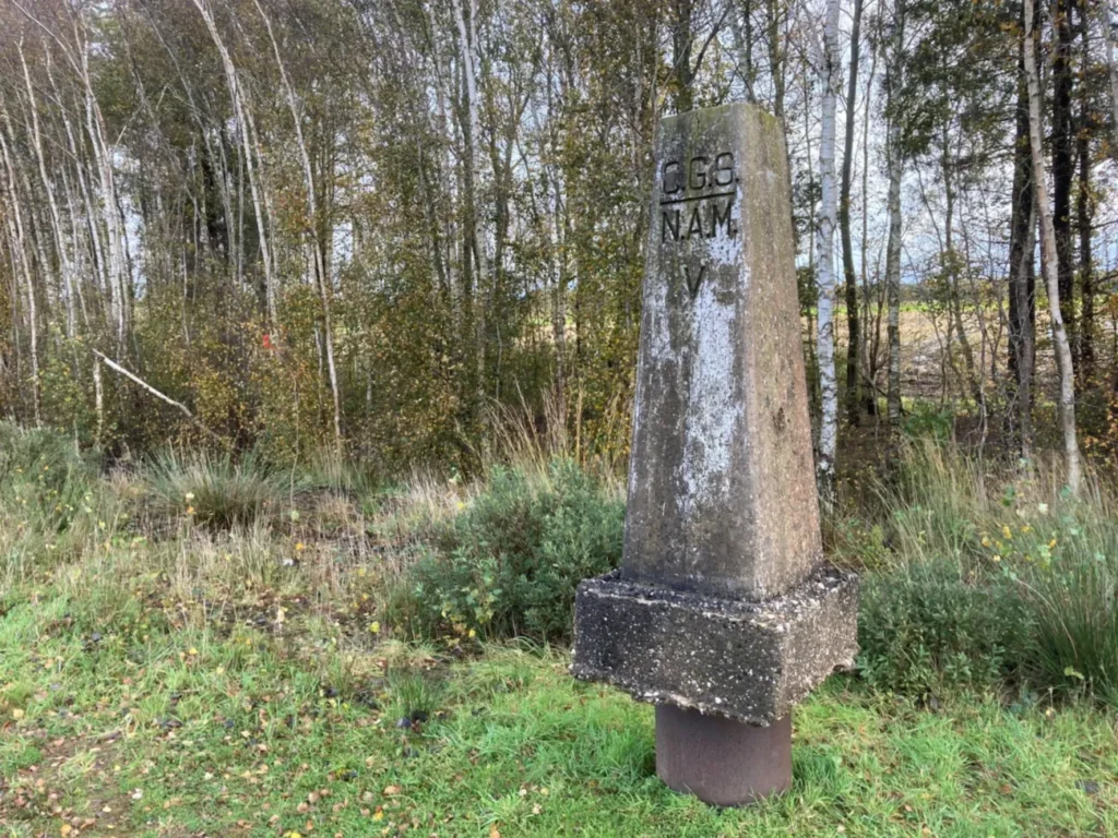 Verwitterter Betonstein mit Aufschrift CGS NAM V steht auf der deutsch-niederländischen Staatsgrenze im Naturpark Moor.