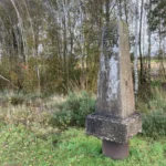 Verwitterter Betonstein mit Aufschrift CGS NAM V steht auf der deutsch-niederländischen Staatsgrenze im Naturpark Moor.
