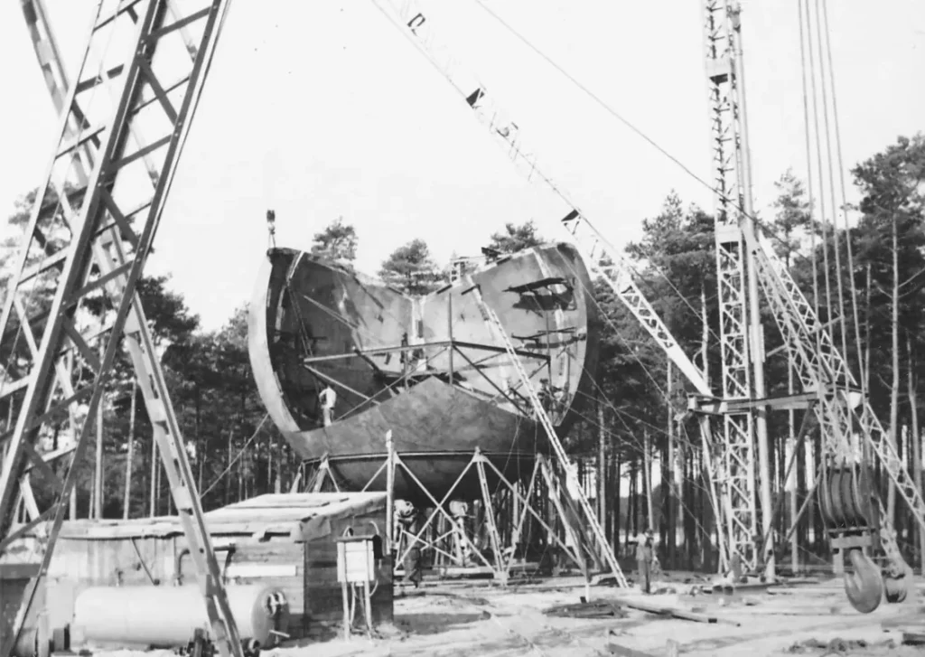 Historische Schwarzweißaufnahme zeigt den Aufbau eines großen Industriebehälters mit Kränen in einem Waldgebiet bei Lingen.