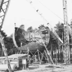 Historische Schwarzweißaufnahme zeigt den Aufbau eines großen Industriebehälters mit Kränen in einem Waldgebiet bei Lingen.