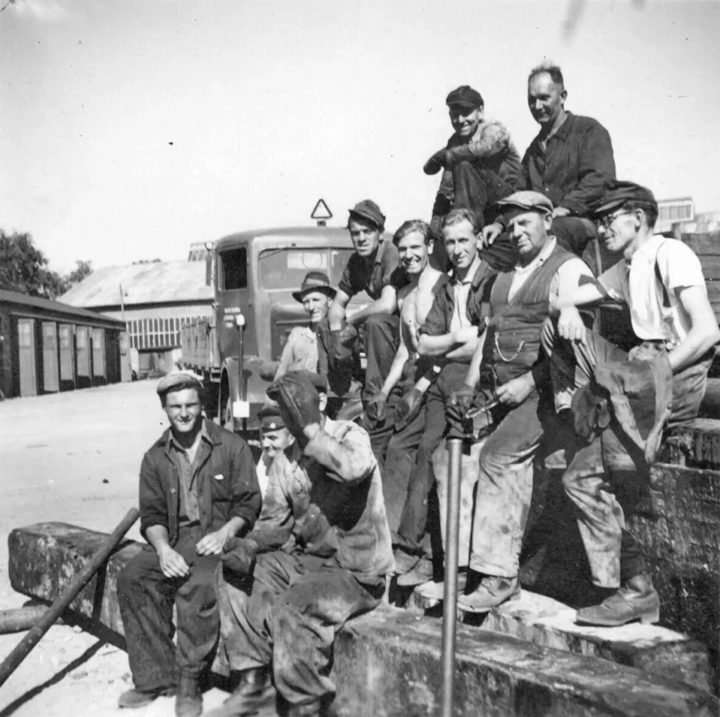 Etwa zehn Arbeiter der Deutschen Schachtbau-Gesellschaft posieren vor einem LKW auf einem Betriebsgelände, ca. 1950er Jahre.