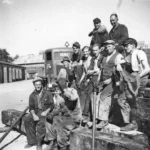 Etwa zehn Arbeiter der Deutschen Schachtbau-Gesellschaft posieren vor einem LKW auf einem Betriebsgelände, ca. 1950er Jahre.