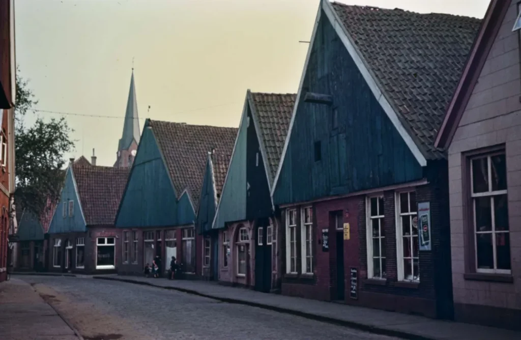 Historische Straßenzeile in Neuenhaus mit markanten Spitzdächern, Backsteinbauten und Kopfsteinpflaster, im Hintergrund ein Kirchturm.