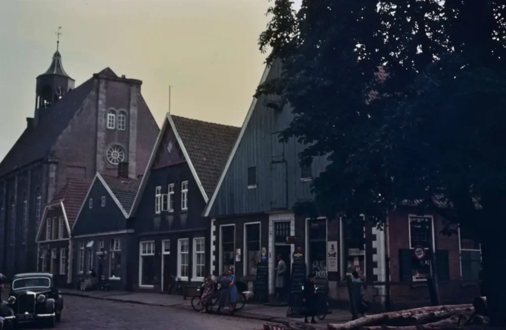 Historische Straßenszene in Neuenhaus mit traditionellen Giebelhäusern, Kirche, Oldtimer und Passanten in den 1950er Jahren.