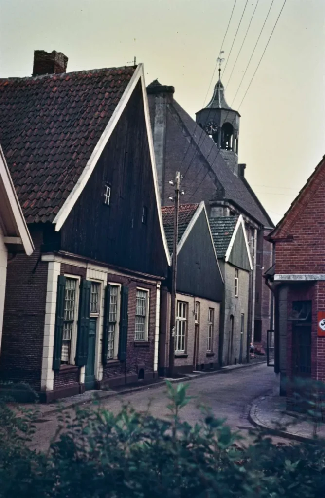 Blick in eine enge Kopfsteinpflasterstraße in Neuenhaus mit Backsteinhäusern und einem Kirchturm im Hintergrund.
