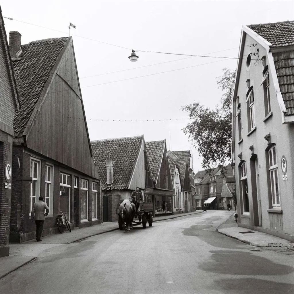 Schwarz-Weiß-Aufnahme einer Straße in Neuenhaus mit Fachwerkhäusern, einem Pferdefuhrwerk und Fußgängern.