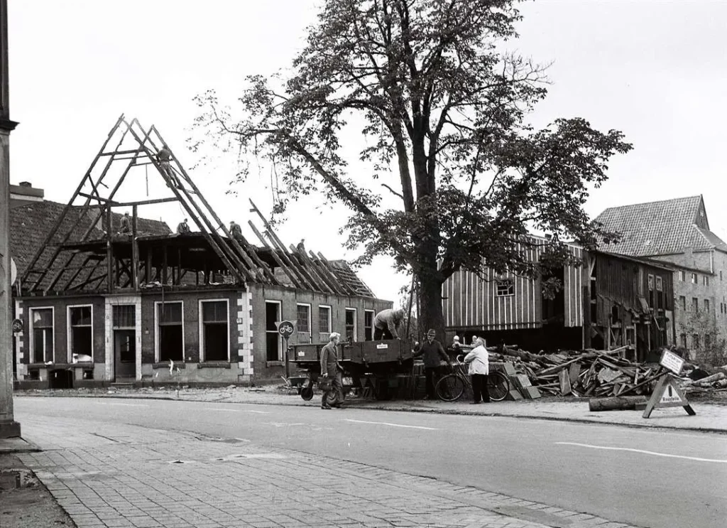 Schwarzweißfoto zeigt den Abriss eines alten Fachwerkhauses in Neuenhaus, während Arbeiter Baumaterial auf einen LKW laden.