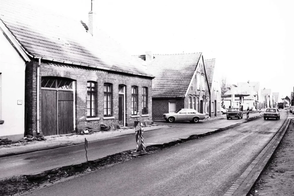 Historische Straße in Neuenhaus mit Backsteingebäuden, Baustellenabsperrung und parkenden Autos der 1970er Jahre.