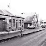 Historische Straße in Neuenhaus mit Backsteingebäuden, Baustellenabsperrung und parkenden Autos der 1970er Jahre.