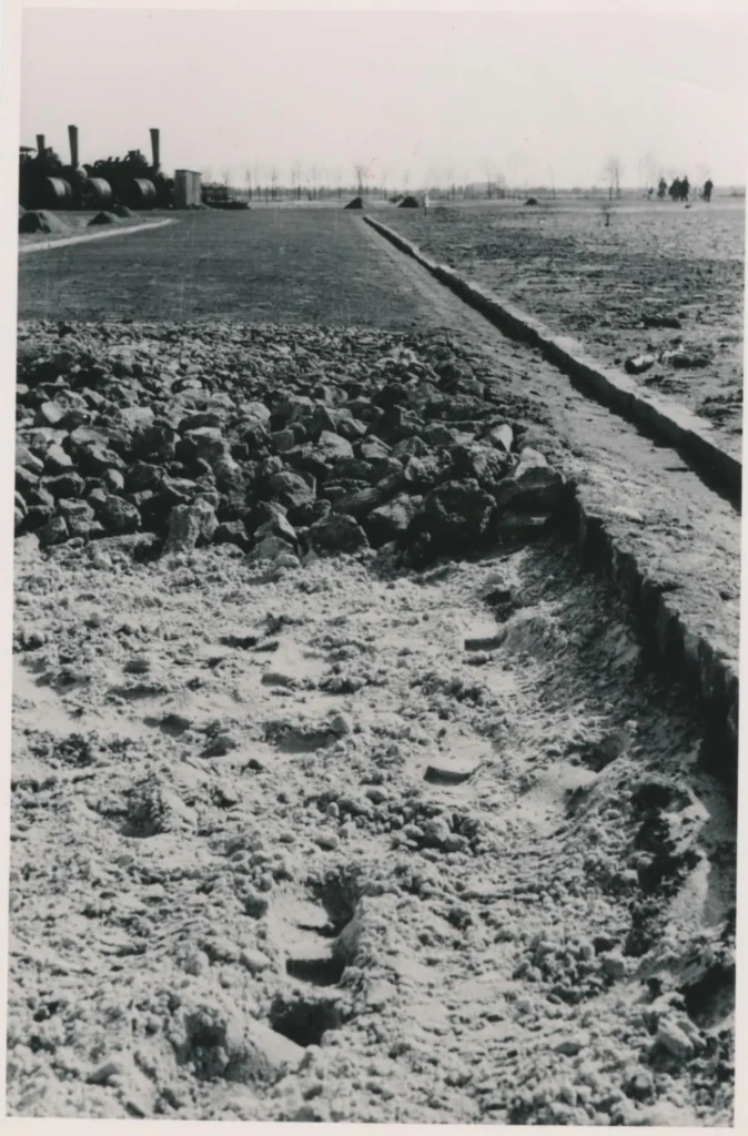Schwarzweißfoto eines Straßenbauprojekts mit Steinen, Graben und Baumaschinen in der Siedlung Walchumer Moor.