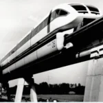 Weißer Transrapid-Triebwagen Nummer 06 fährt auf einer Betonhochtrasse über flaches Emsland.