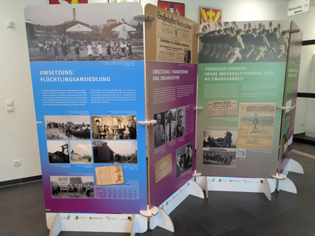 Drei Ausstellungstafeln zur Geschichte des Emslandplans mit historischen Fotos und deutschen Texten über Flüchtlingsansiedlung und NS-Zwangsarbeit.