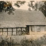 Altes, baufälliges Fachwerkgebäude mit Ziegeldach und einem Motorrad davor, umgeben von verwildertem Garten.