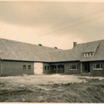 Historische Aufnahme eines frisch errichteten Aussiedlerhofs aus Backstein mit weitläufigem Satteldach auf unbebautem Gelände.