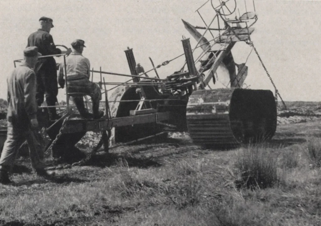 Drei Arbeiter bedienen den holländischen Tiefpflug Gigant bei der Moorkultivierung, historische Schwarzweißaufnahme.