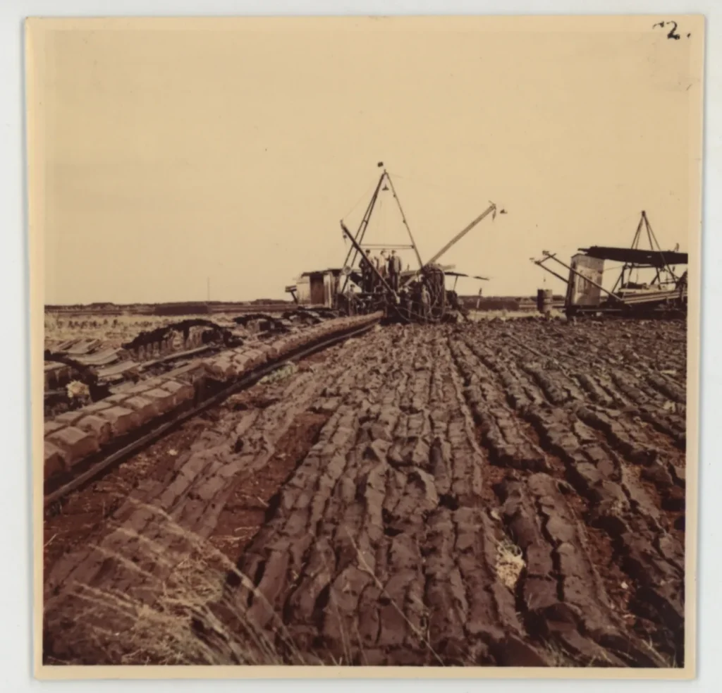 Historische Aufnahme von Torfabbaumaschinen auf einem weitläufigen, gefurchten Torffeld im Emsland.