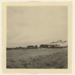 Schwarzweißfoto einer flachen Emslandlandschaft mit Fabrikgebäuden, rauchenden Schornsteinen und Bäumen am Horizont.