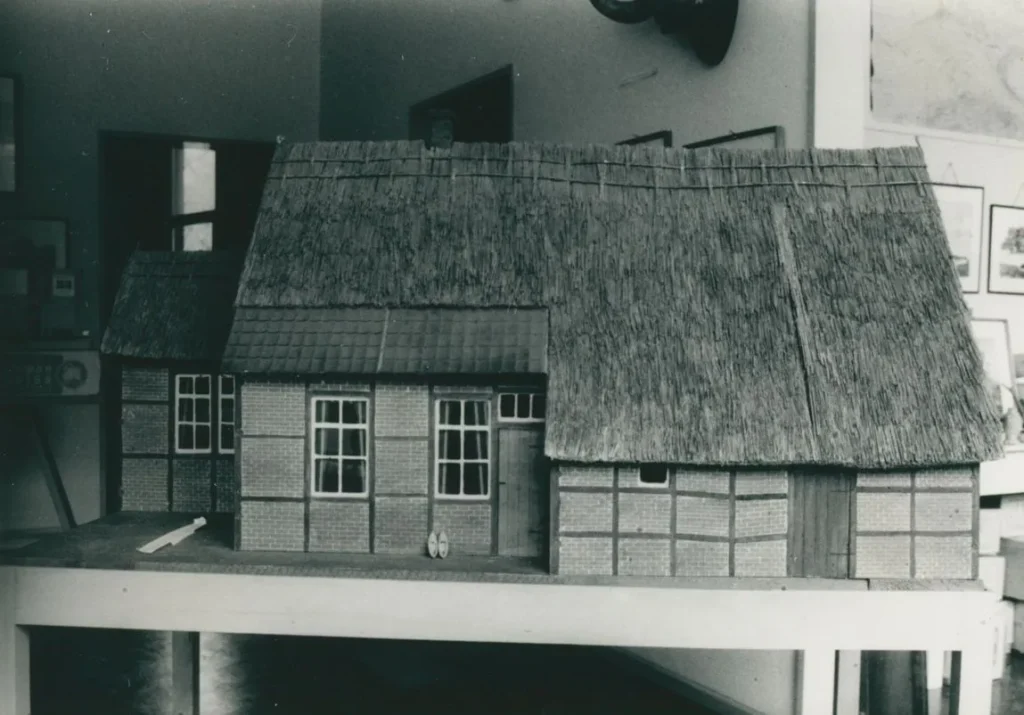 Detailliertes Architekturmodell eines emsländischen Fachwerkhauses mit Reetdach auf einem Ausstellungstisch.