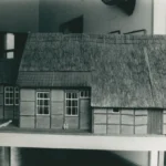 Detailliertes Architekturmodell eines emsländischen Fachwerkhauses mit Reetdach auf einem Ausstellungstisch.