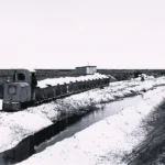 Eine Schmalspurbahn transportiert helles Material entlang eines Grabens durch flaches Moorland beim Straßenbau im Emsland.
