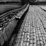 Historische Schwarzweißaufnahme von maschinellem Torfabbau im Emsland mit Förderbahn und gestapelten Torfziegeln.